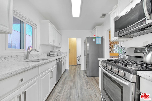 kitchen with appliances with stainless steel finishes, white cabinets, light stone counters, and sink