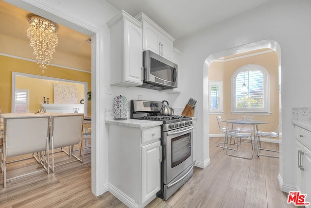 kitchen with white cabinets, stainless steel appliances, light hardwood / wood-style floors, a chandelier, and light stone counters