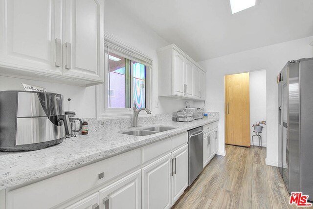 kitchen with stainless steel appliances, white cabinets, light hardwood / wood-style flooring, light stone counters, and sink