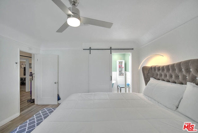 bedroom with ceiling fan, a barn door, and hardwood / wood-style floors