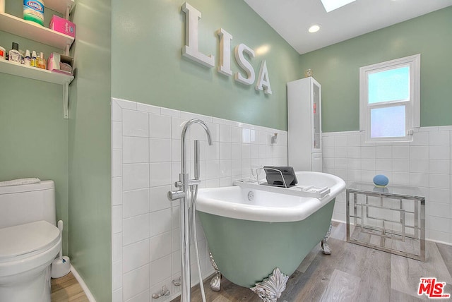 bathroom featuring hardwood / wood-style flooring, a washtub, tile walls, and toilet