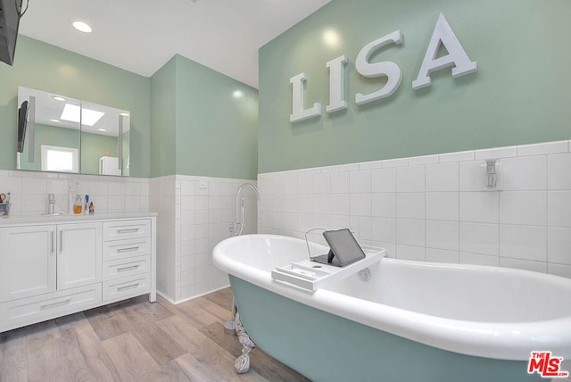 bathroom featuring hardwood / wood-style floors, tile walls, a washtub, and vanity