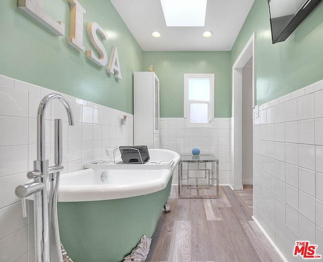 bathroom with hardwood / wood-style flooring, tile walls, a tub, and a skylight