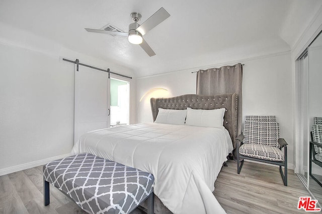 bedroom featuring a closet, light hardwood / wood-style floors, a barn door, and ceiling fan