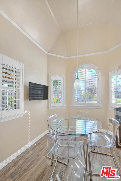 dining area with high vaulted ceiling, a healthy amount of sunlight, wood-type flooring, and crown molding