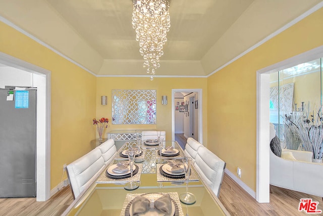 dining space with light hardwood / wood-style flooring, a raised ceiling, and an inviting chandelier