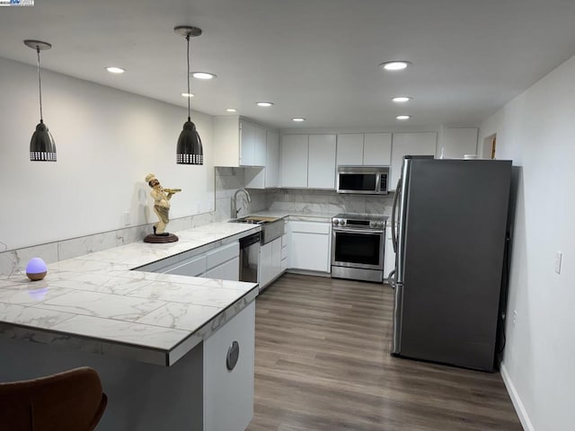 kitchen featuring kitchen peninsula, stainless steel appliances, pendant lighting, and white cabinets