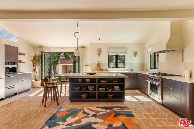 kitchen featuring double oven range, ventilation hood, tasteful backsplash, hanging light fixtures, and a center island