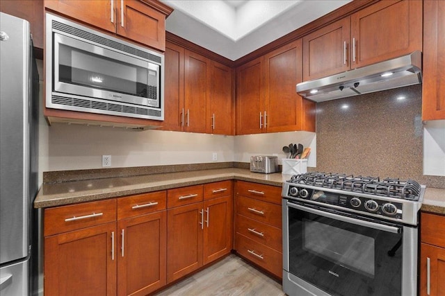 kitchen with light stone counters, appliances with stainless steel finishes, decorative backsplash, and light wood-type flooring