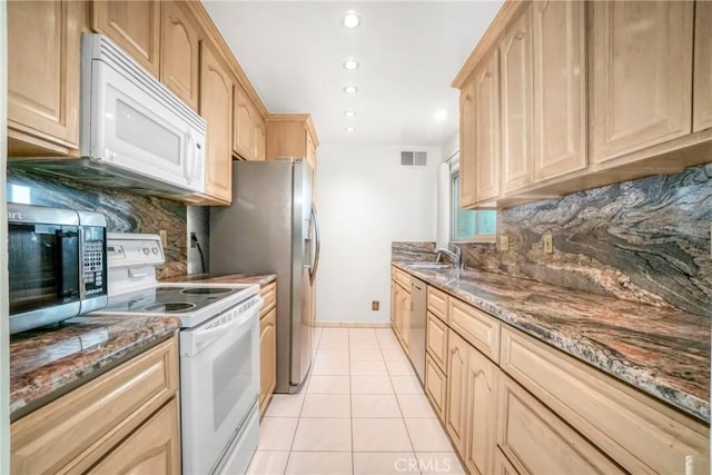 kitchen featuring appliances with stainless steel finishes, backsplash, light brown cabinetry, dark stone countertops, and sink