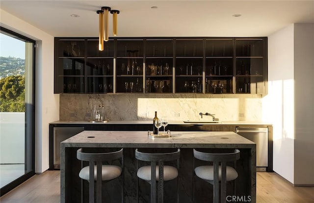 bar with sink, backsplash, dishwasher, and light hardwood / wood-style flooring