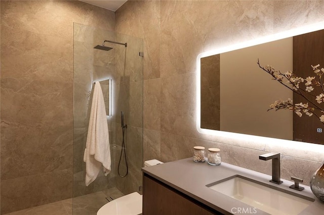 bathroom featuring vanity, toilet, tile walls, and tiled shower