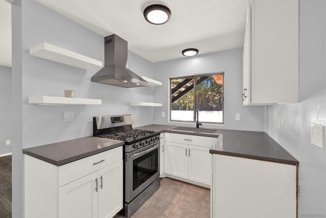 kitchen featuring wall chimney range hood, gas stove, sink, light tile patterned flooring, and white cabinetry