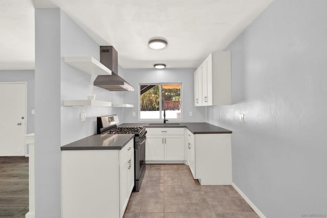 kitchen featuring wall chimney range hood, gas stove, sink, light tile patterned floors, and white cabinets