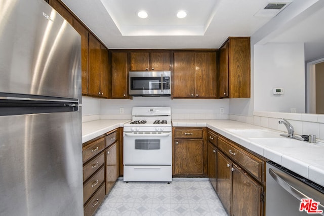 kitchen featuring sink, appliances with stainless steel finishes, a raised ceiling, and tile counters