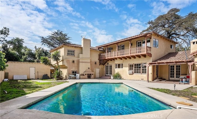 rear view of property featuring french doors, a chimney, a balcony, and stucco siding