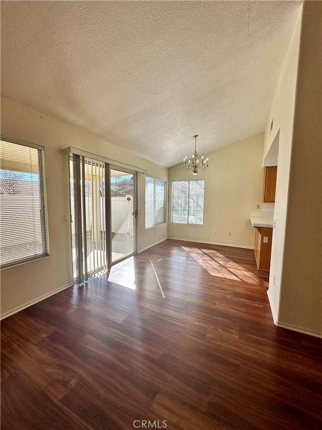 unfurnished living room featuring a wealth of natural light, dark hardwood / wood-style flooring, a chandelier, and vaulted ceiling