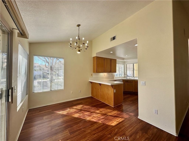 kitchen with lofted ceiling, a notable chandelier, kitchen peninsula, sink, and dark wood-type flooring