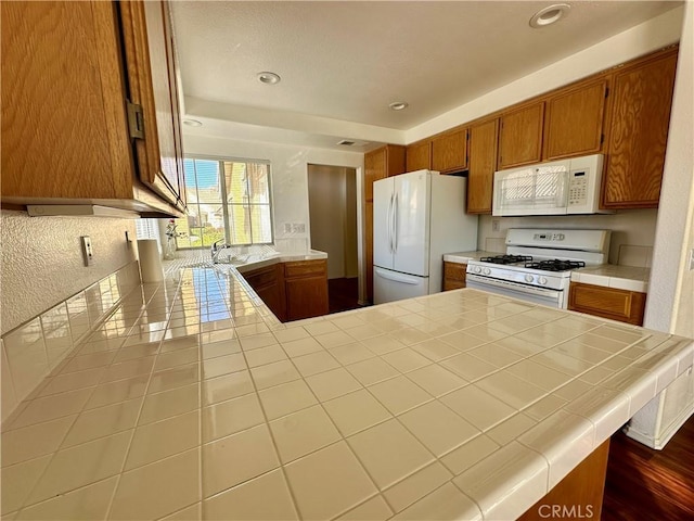 kitchen featuring tile counters, kitchen peninsula, sink, and white appliances