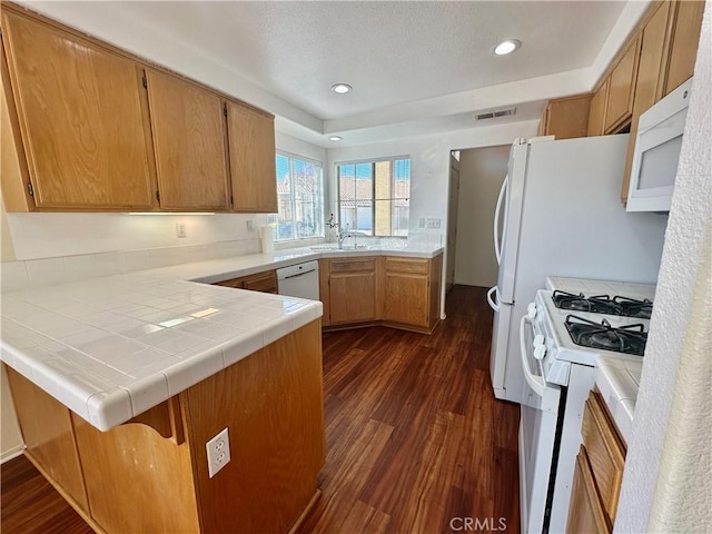 kitchen with tile countertops, kitchen peninsula, white appliances, dark wood-type flooring, and sink