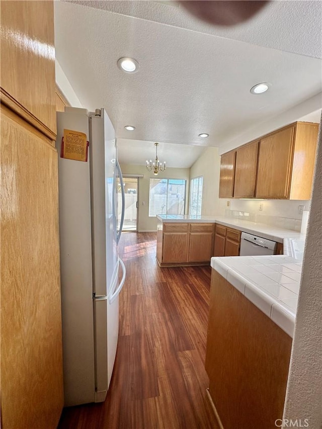 kitchen featuring dishwasher, kitchen peninsula, dark wood-type flooring, white refrigerator, and a chandelier