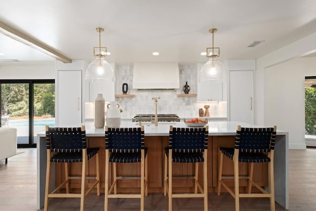 kitchen featuring custom range hood, hanging light fixtures, backsplash, and white cabinets