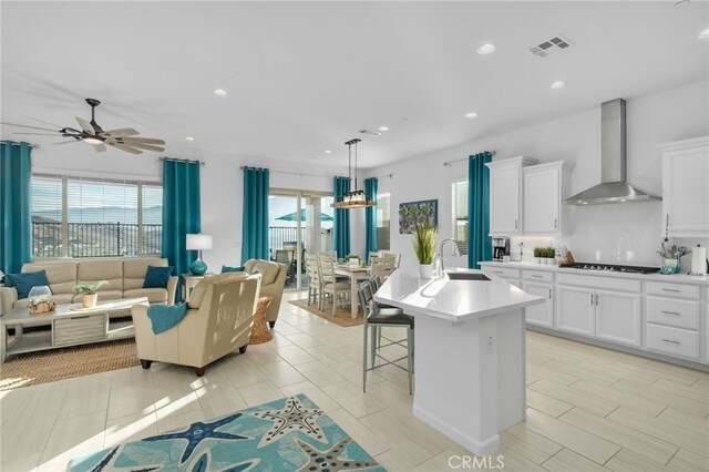 kitchen featuring sink, wall chimney range hood, white cabinets, and an island with sink