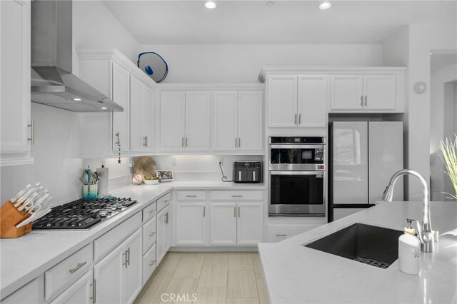 kitchen featuring stainless steel appliances, wall chimney exhaust hood, white cabinets, and sink