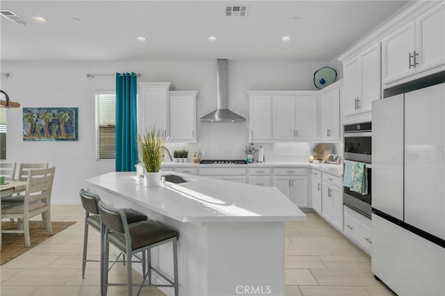 kitchen featuring white fridge, white cabinetry, stainless steel double oven, wall chimney exhaust hood, and a center island