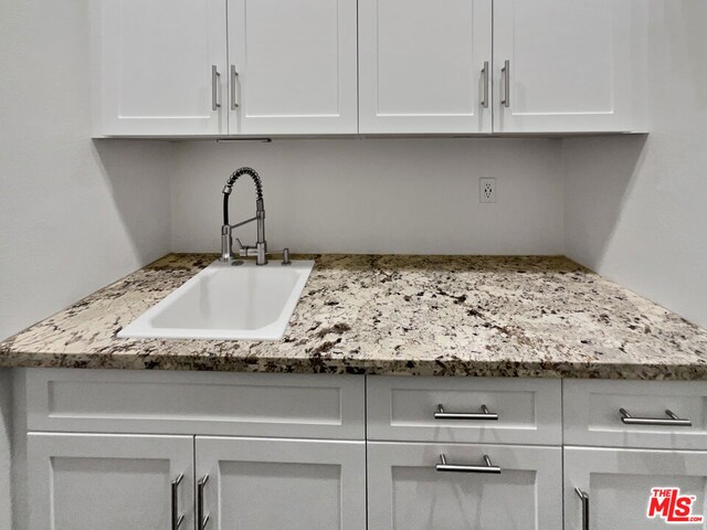 kitchen with sink, light stone counters, and white cabinetry