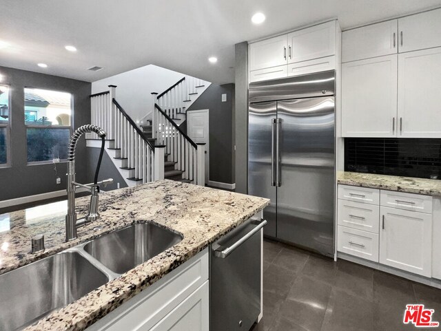 kitchen featuring white cabinetry, stainless steel appliances, tasteful backsplash, sink, and light stone counters