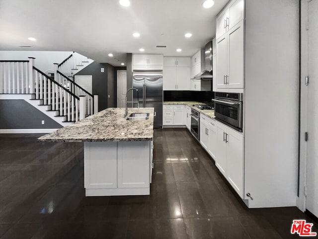 kitchen featuring appliances with stainless steel finishes, wall chimney exhaust hood, white cabinetry, sink, and light stone counters