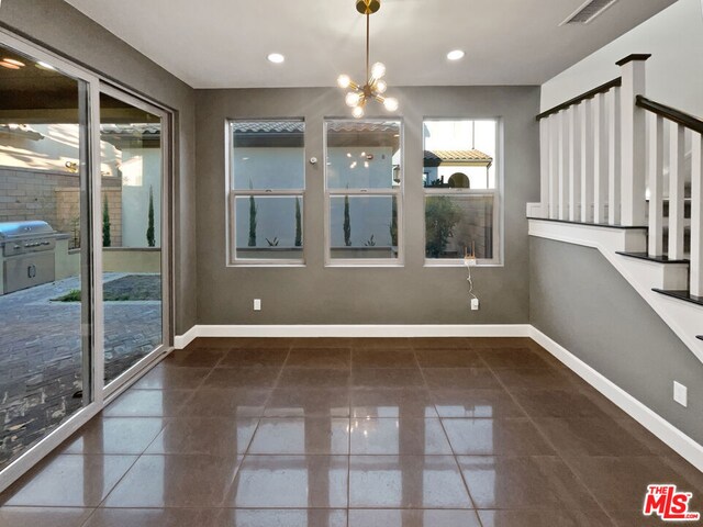 unfurnished dining area with dark tile patterned flooring and an inviting chandelier