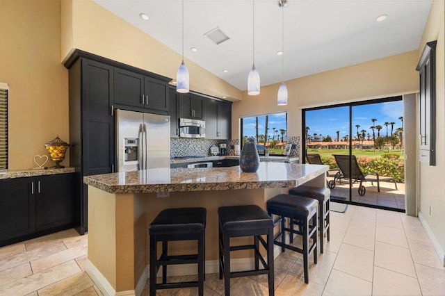 kitchen featuring appliances with stainless steel finishes, pendant lighting, dark stone countertops, and an island with sink