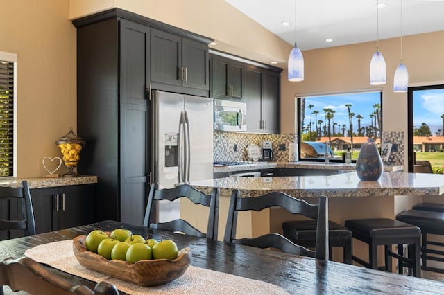 kitchen with stainless steel fridge, a breakfast bar area, backsplash, decorative light fixtures, and dark stone countertops