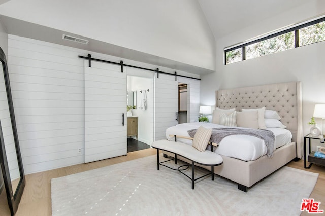 bedroom featuring ensuite bathroom, a barn door, hardwood / wood-style floors, and high vaulted ceiling