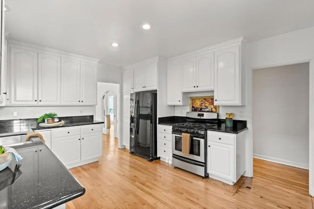 kitchen featuring gas stove, black refrigerator, white cabinets, and light hardwood / wood-style flooring