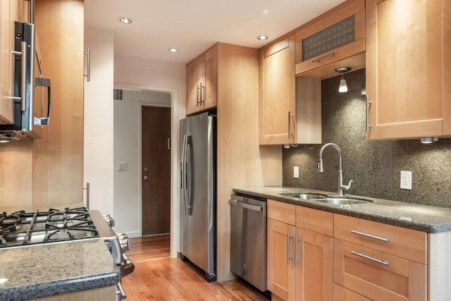 kitchen featuring sink, dark stone countertops, stainless steel appliances, light hardwood / wood-style floors, and decorative backsplash