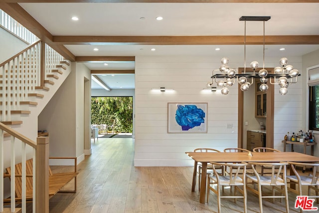 dining area featuring light wood-type flooring, a notable chandelier, beamed ceiling, and wooden walls