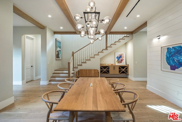 dining room featuring wood walls, an inviting chandelier, beamed ceiling, and light wood-type flooring