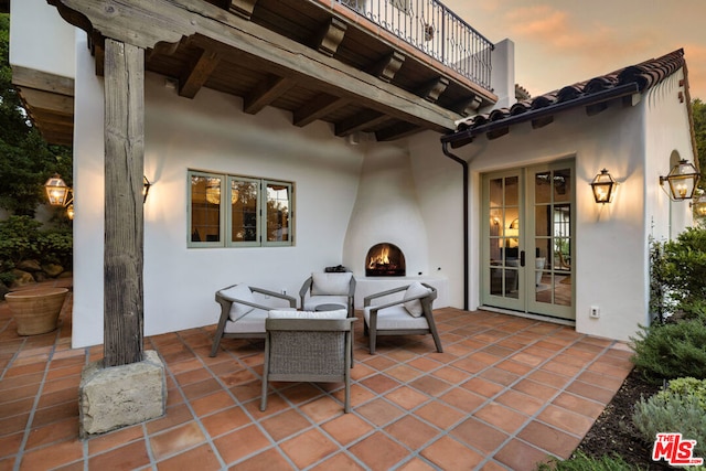 patio terrace at dusk featuring a large fireplace, french doors, and a balcony