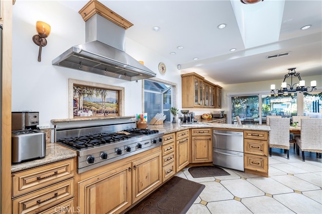 kitchen with kitchen peninsula, an inviting chandelier, stainless steel gas cooktop, island range hood, and light stone counters