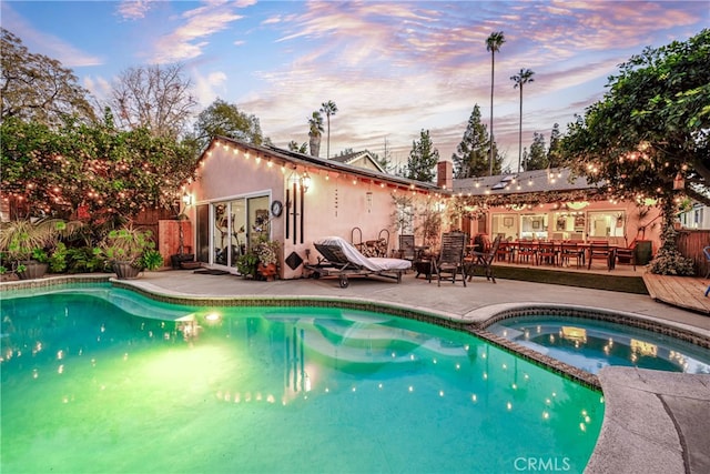 pool at dusk with a patio area and an in ground hot tub