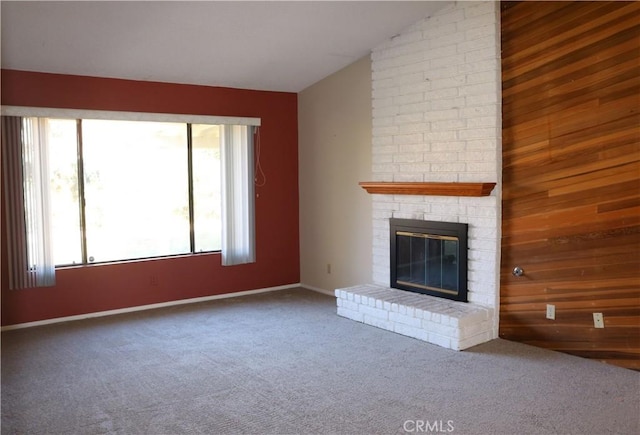 unfurnished living room featuring a fireplace, a healthy amount of sunlight, wooden walls, and carpet