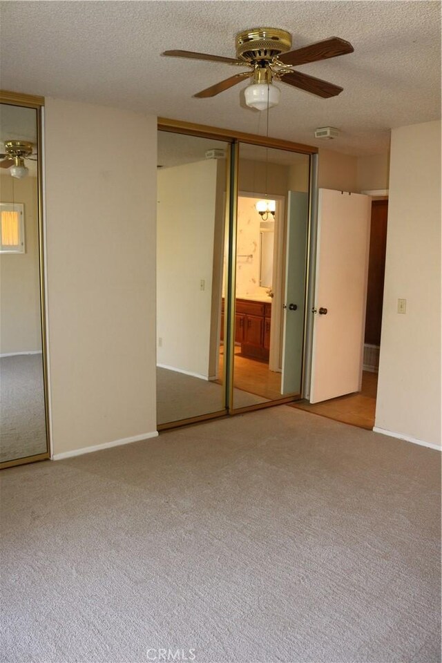 unfurnished bedroom featuring carpet flooring, ensuite bath, a textured ceiling, ceiling fan, and a closet