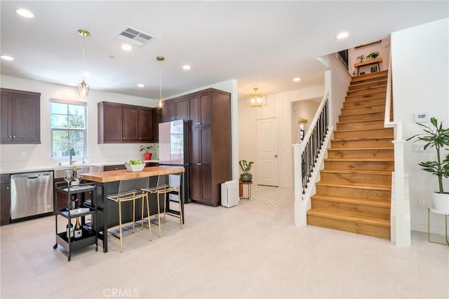 kitchen with fridge, decorative light fixtures, stainless steel dishwasher, dark brown cabinetry, and a center island