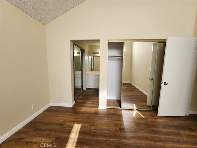 unfurnished bedroom with dark hardwood / wood-style floors, ensuite bath, a closet, lofted ceiling, and a textured ceiling