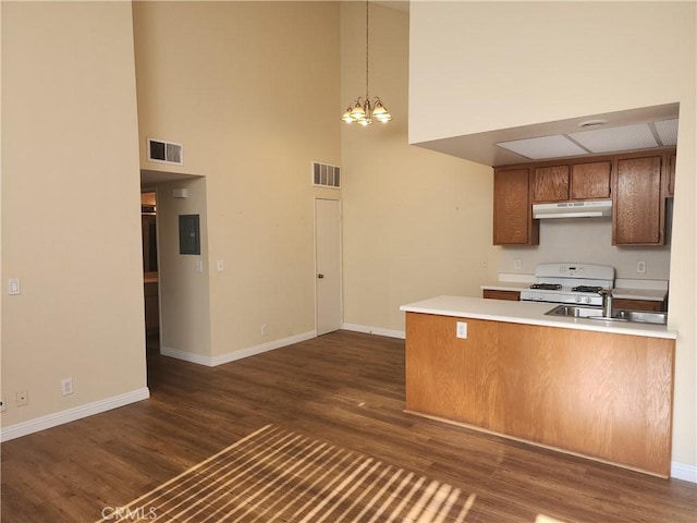 kitchen with a towering ceiling, decorative light fixtures, kitchen peninsula, a chandelier, and white range with gas stovetop