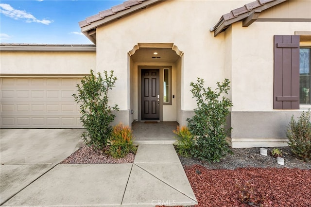 view of exterior entry featuring stucco siding, concrete driveway, a tile roof, and a garage