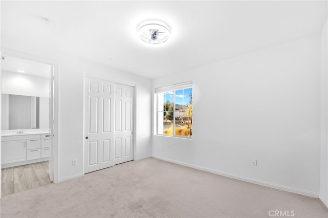 unfurnished bedroom featuring connected bathroom, light colored carpet, a closet, and baseboards